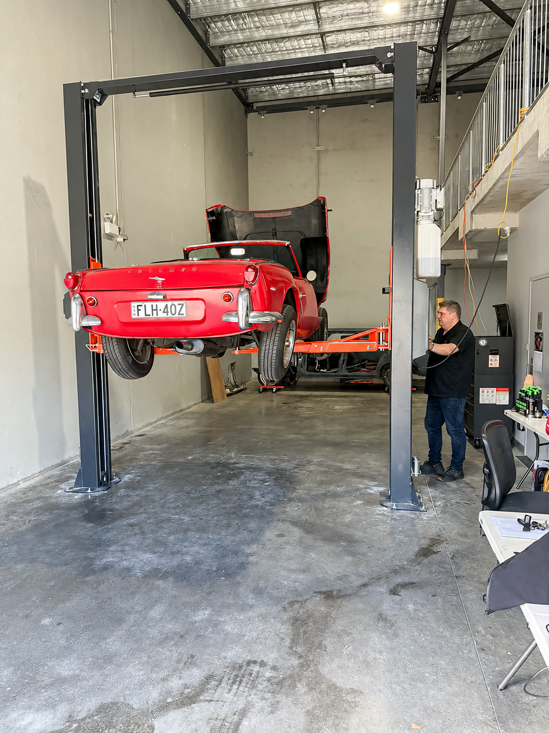 A Triumph raised on the hoist with a workshop user alongside.