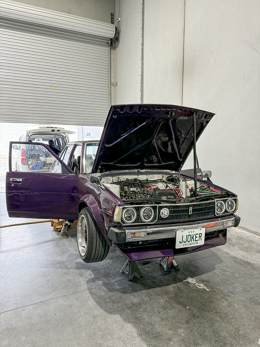 A classic car with its bonnet open in the workshop.